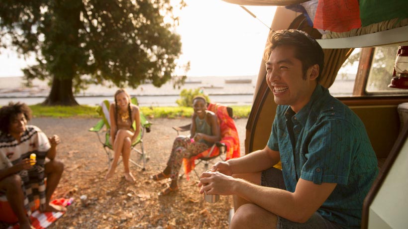 Lachende man zit met vrienden bij camper