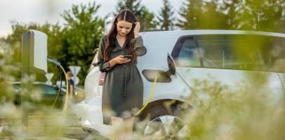 Een vrouw staat met telefoon in haar handen voor een witte elektrische auto