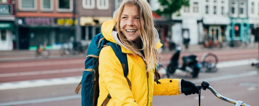 Een afbeelding van een lachende vrouw in een gele jas die op de fiets zit.  Een afbeelding van een lachende vrouw in een gele jas die op de fiets zit.