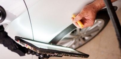 Een wit voertuig met een hand die een geel voorwerp vasthoudt vlakbij een wiel