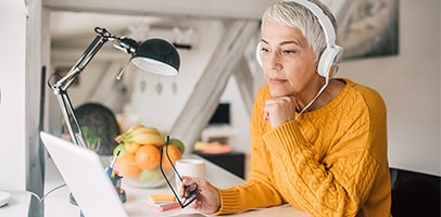 Vrouw met gele trui en koptelefoon kijkt naar laptop Vrouw met gele trui en koptelefoon kijkt naar laptop